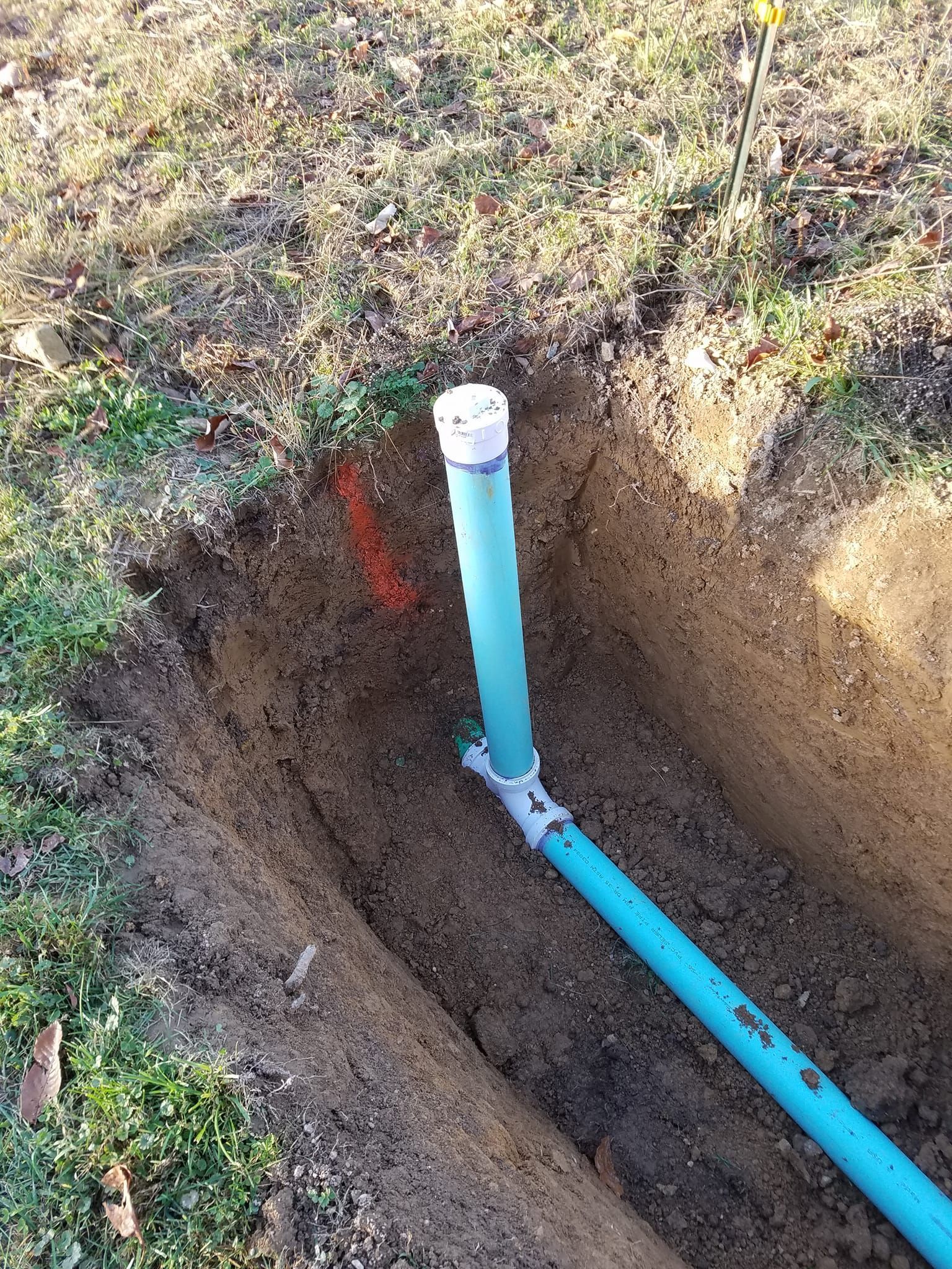 Blue PVC pipes emerging from a trench in the dirt, capped with white, likely for plumbing or irrigation.