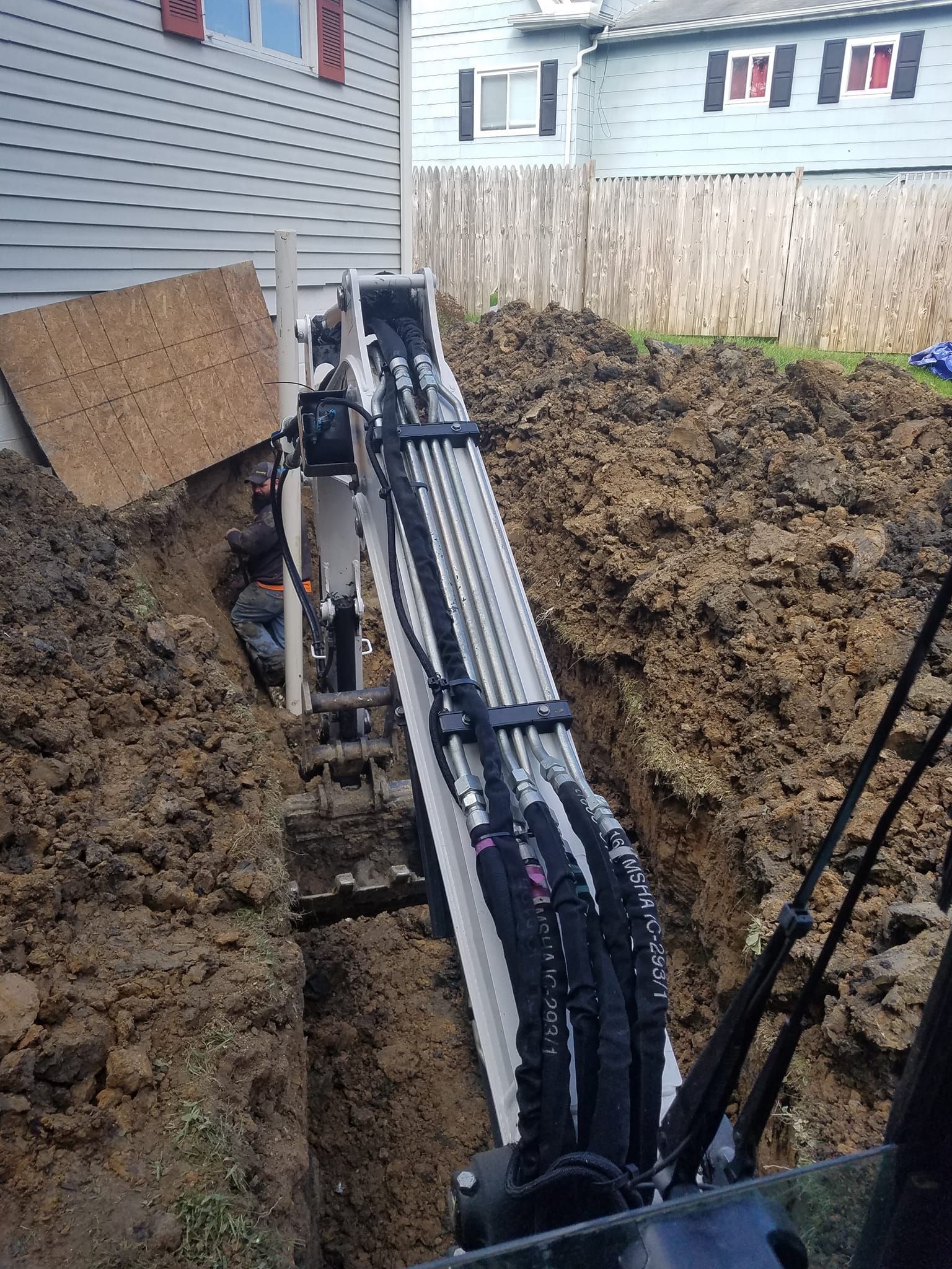 An excavator digging a trench next to a house.