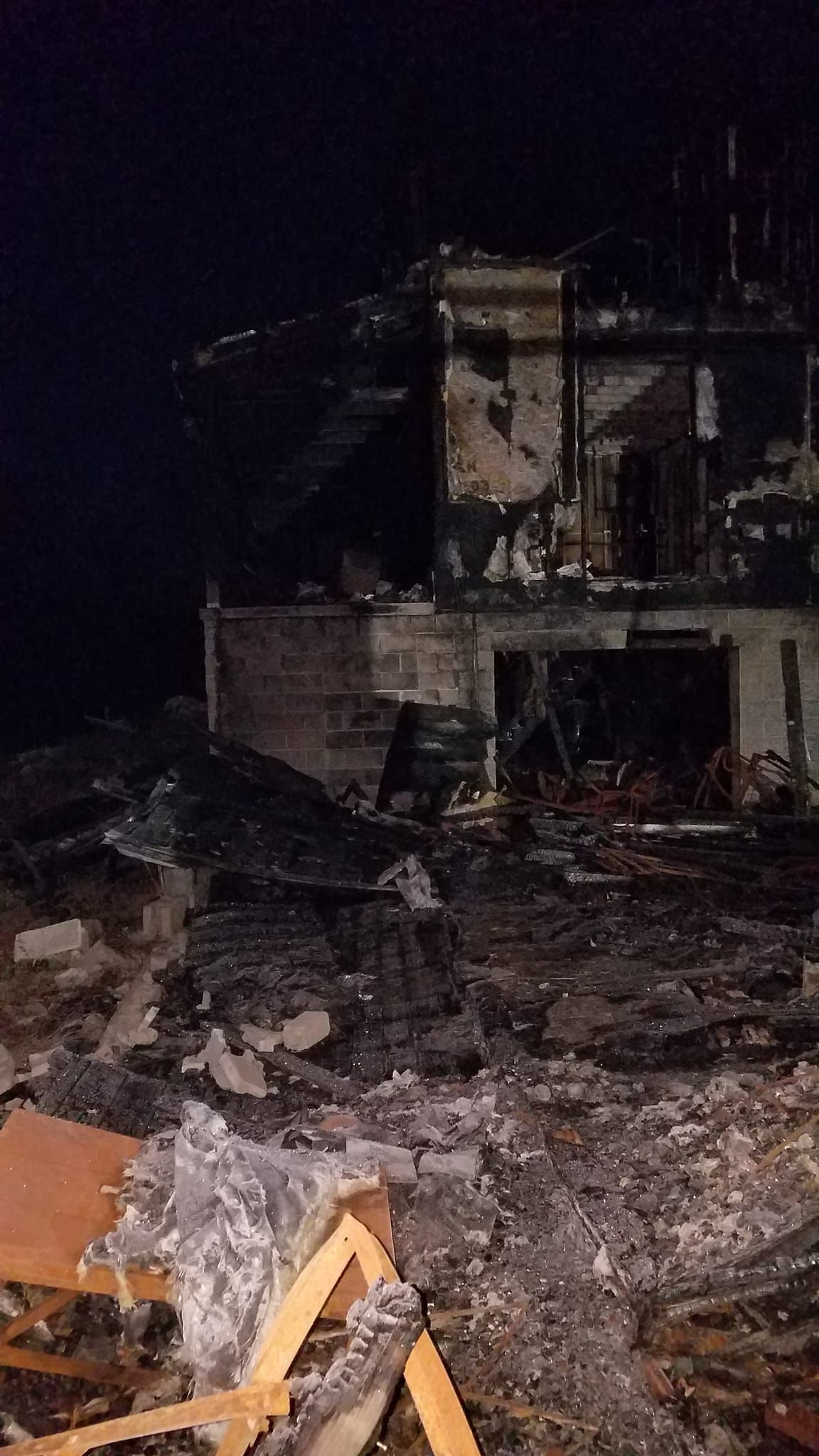 Charred remains of a building at night. Visible debris and structural damage from a fire.