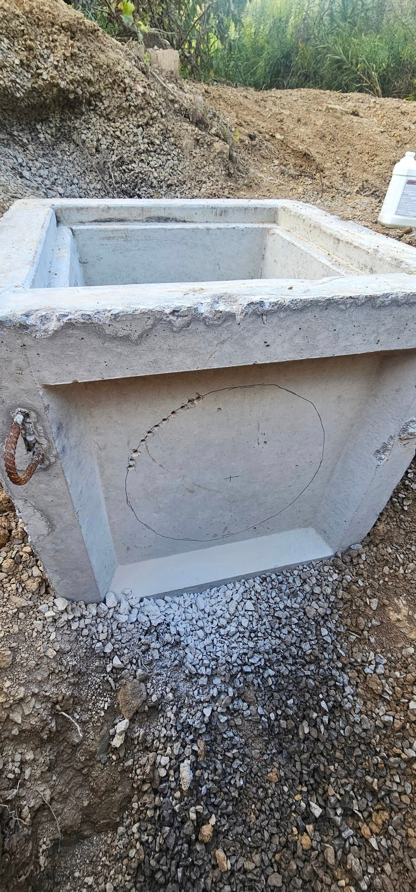 Concrete structure set in gravel and dirt. A curved outline is on the side of the structure.