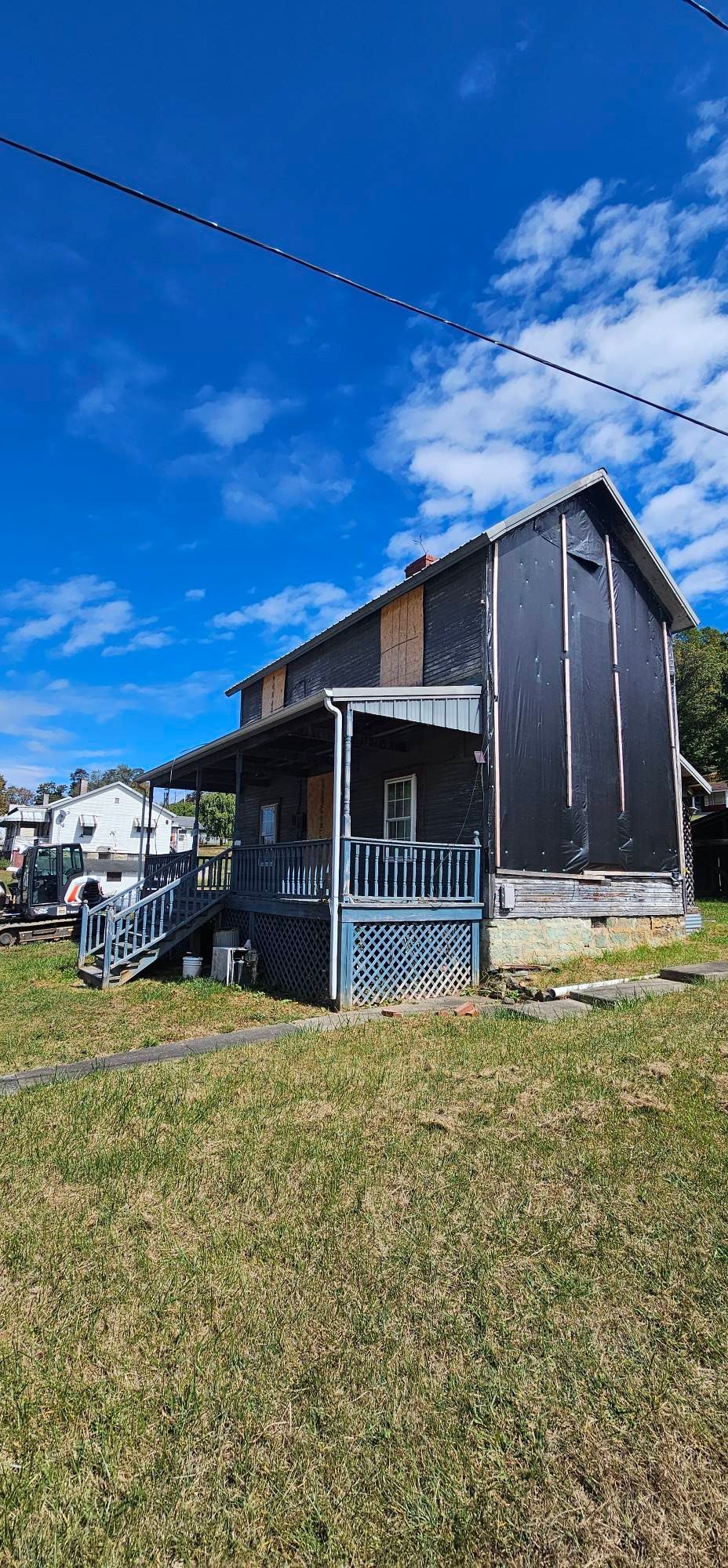 Exterior view of a weathered two-story house with a porch and steps. Blue sky.