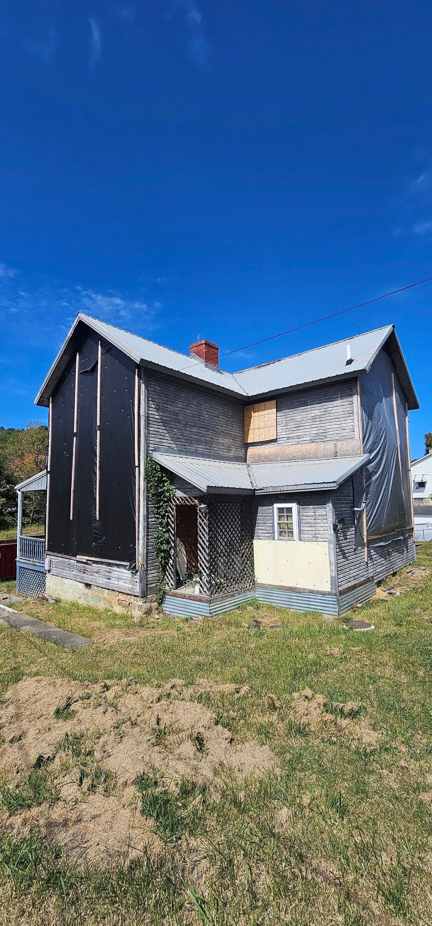 Dilapidated two-story house with gray weathered siding and a red brick chimney under a clear blue sky.