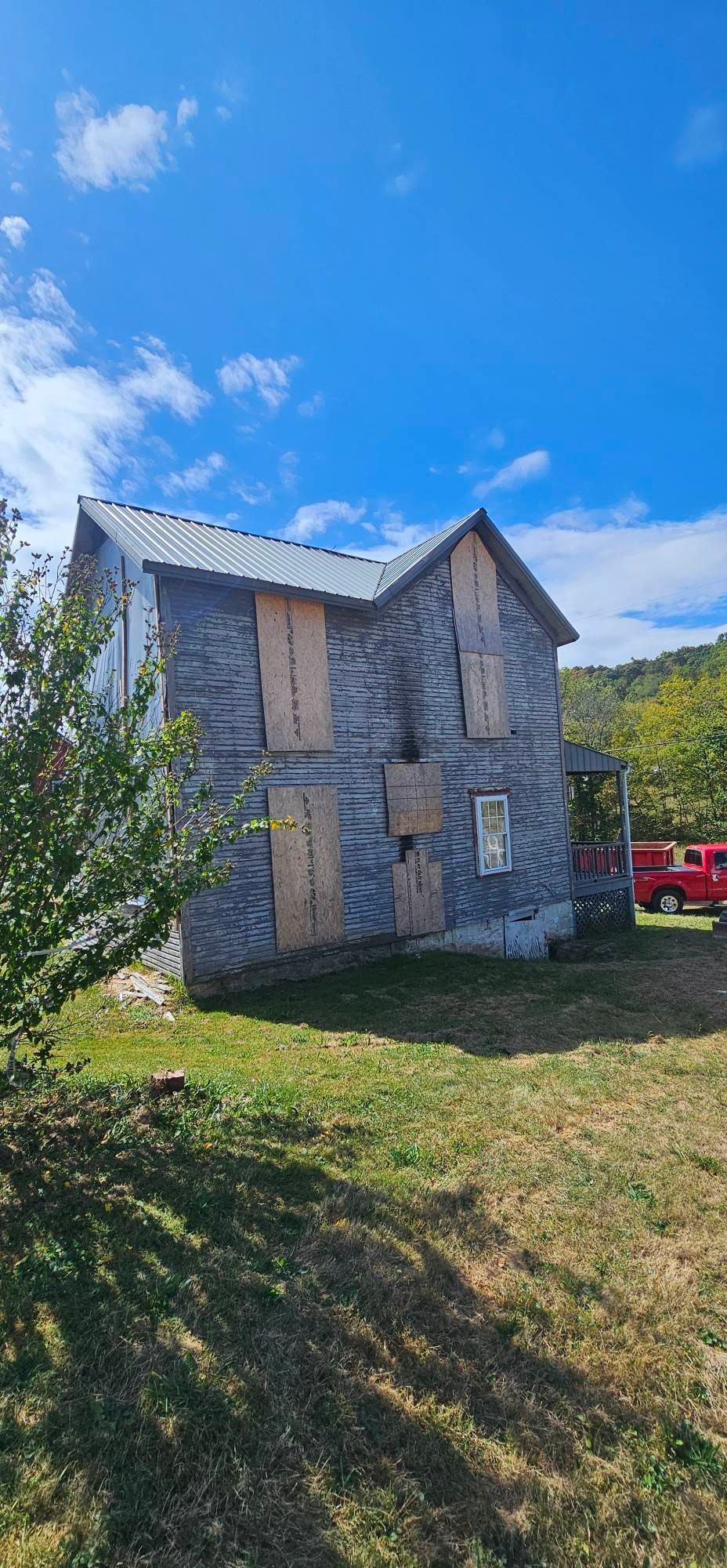 Weathered two-story house with boarded-up windows under a blue sky.