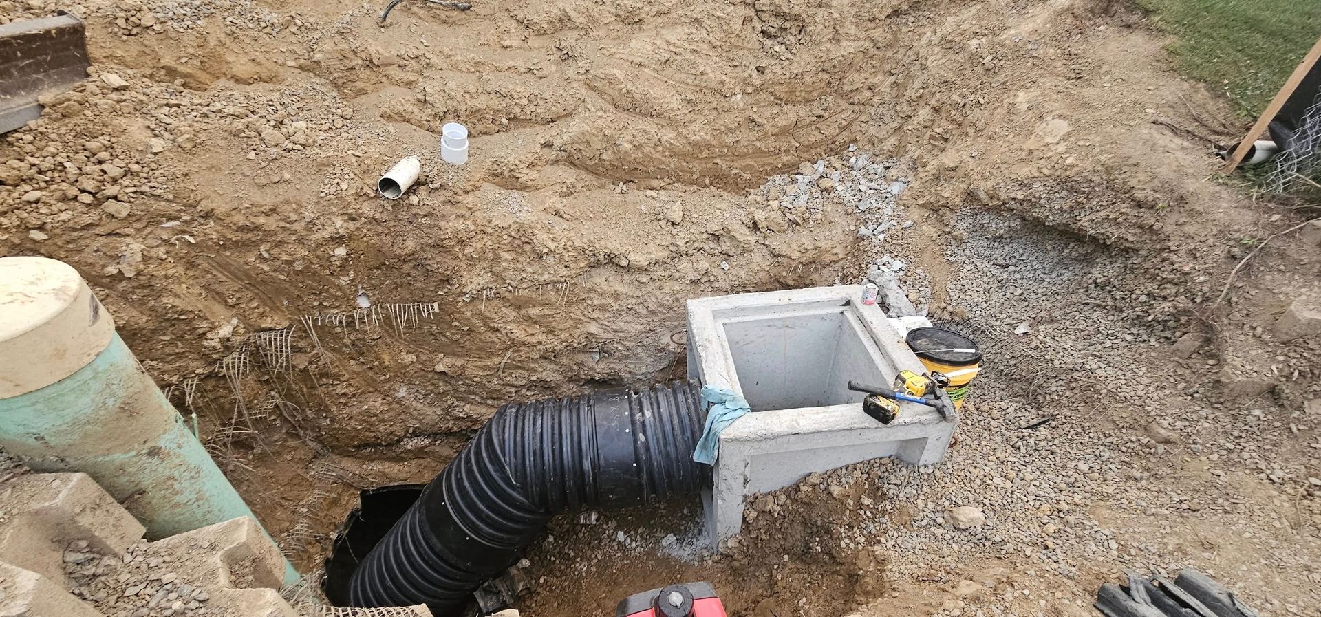 Construction site with a concrete drainage box, corrugated pipe, and excavated earth.