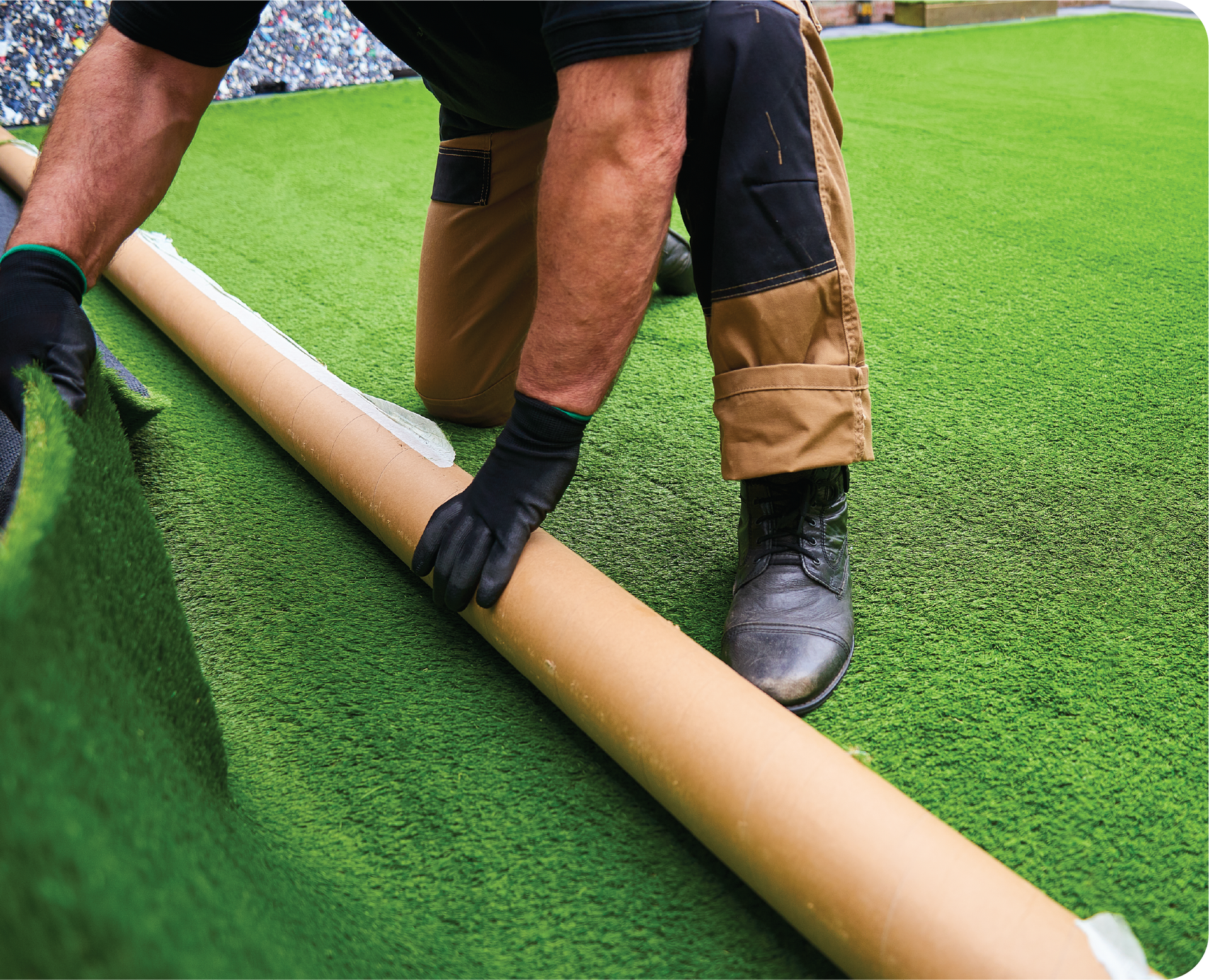 A man is kneeling down holding a roll of artificial grass.
