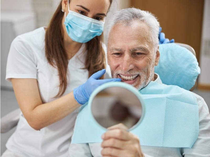 Dentist showing a patient his teeth with a mirror. Both are smiling.