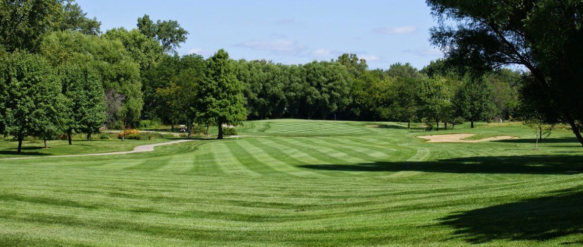 A lush green golf course surrounded by trees on a sunny day.