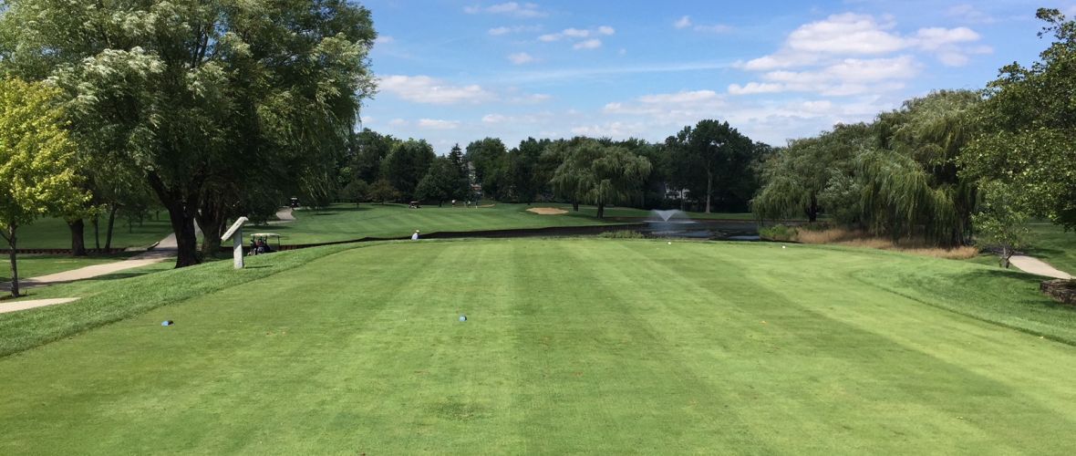 A golf course with a lot of grass and trees on a sunny day.