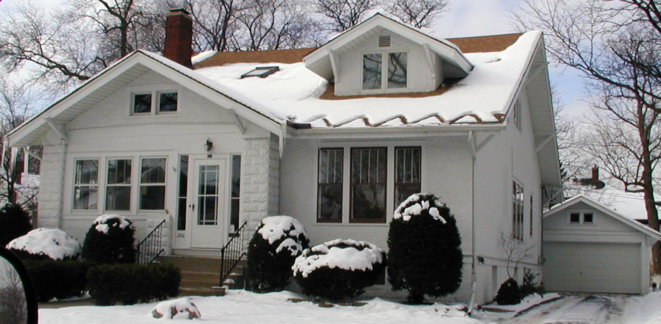 A white house with snow on the ground and trees in the background