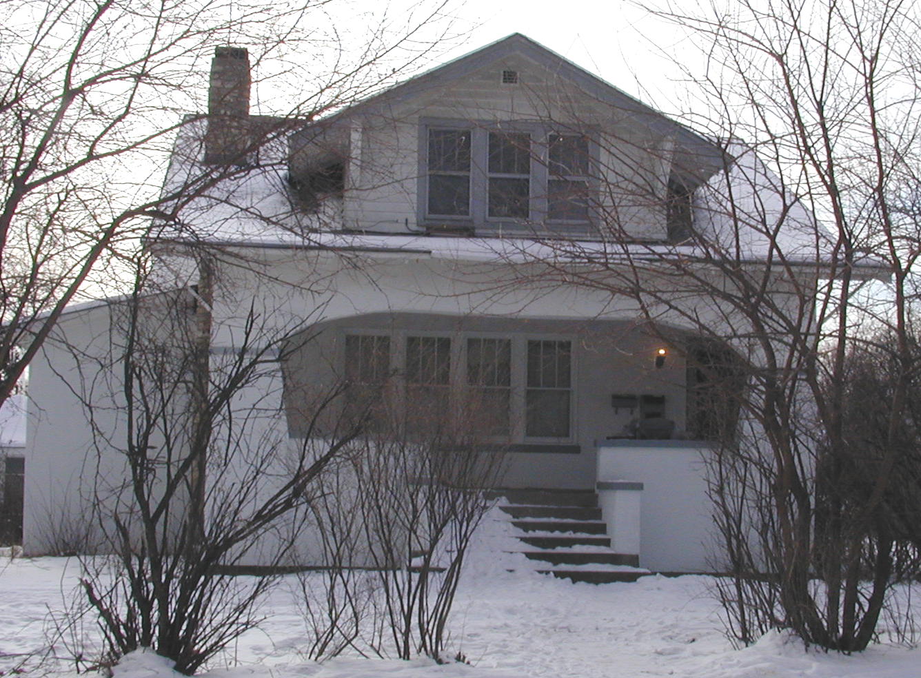 A white house with a porch and stairs in the snow