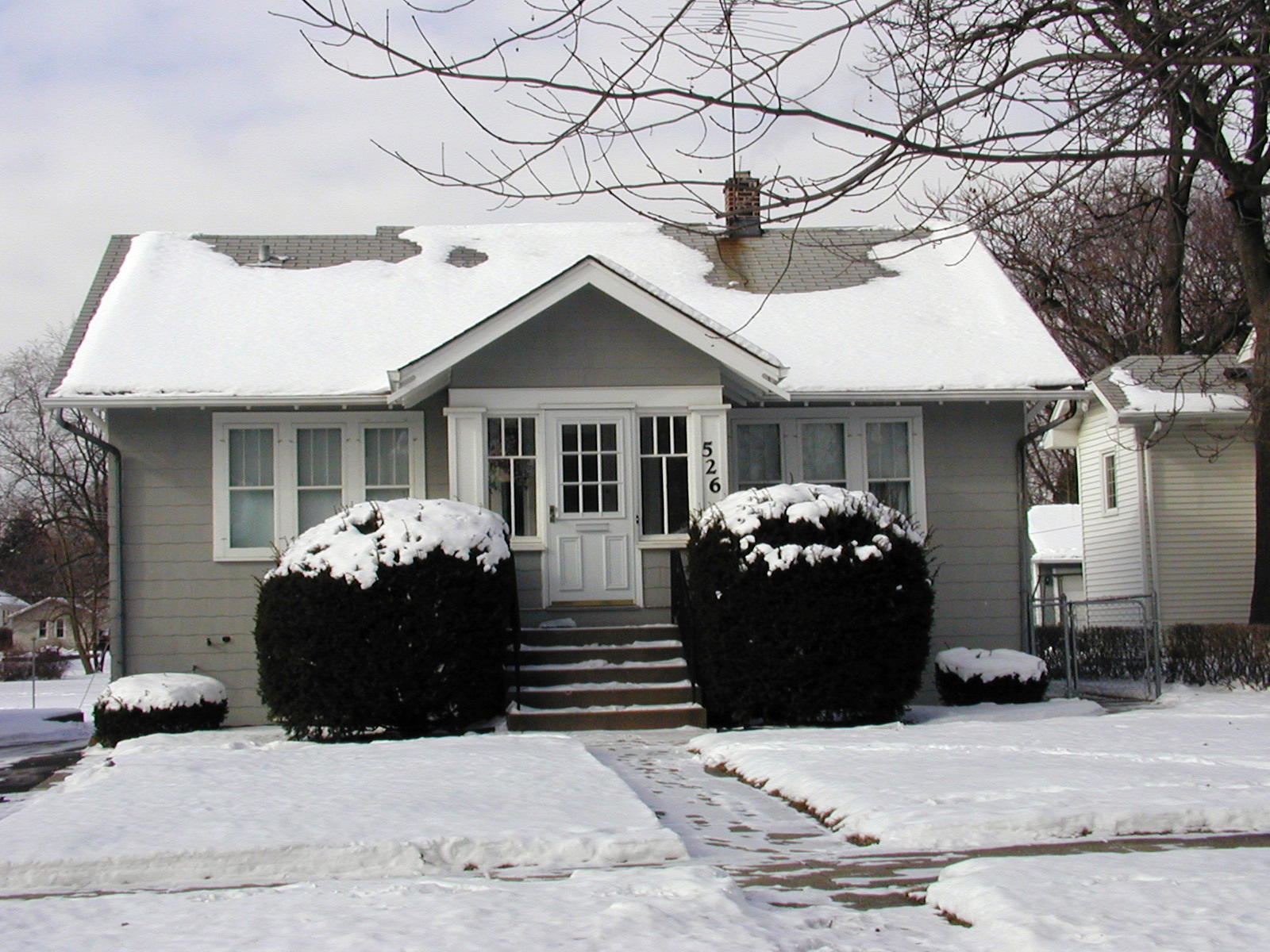 A snowy house with bushes in front of it
