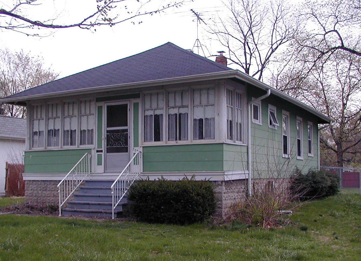 A small green house with a porch and stairs