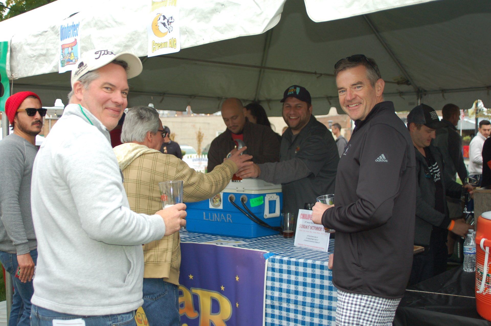 A group of men are standing under a tent drinking beer
