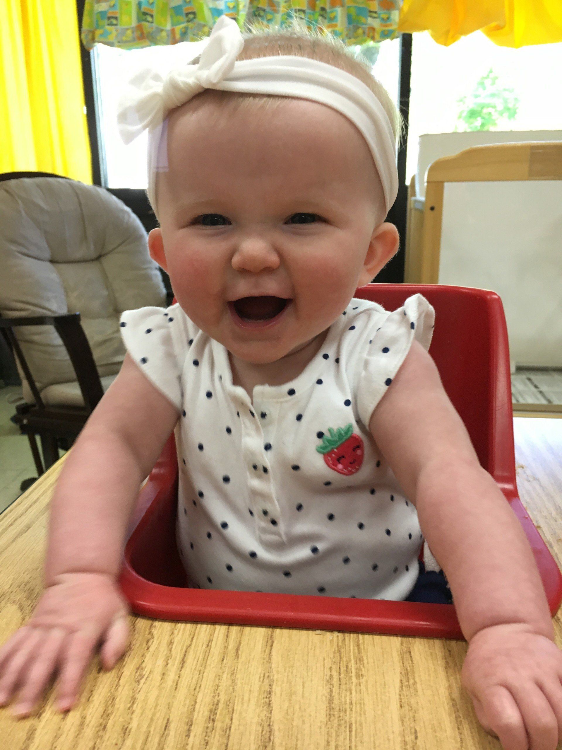A baby is sitting in a high chair and smiling