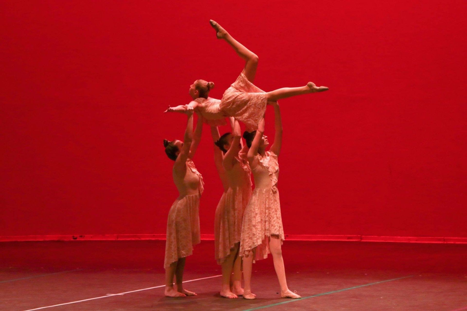 A group of dancers are performing on a stage with a red background.