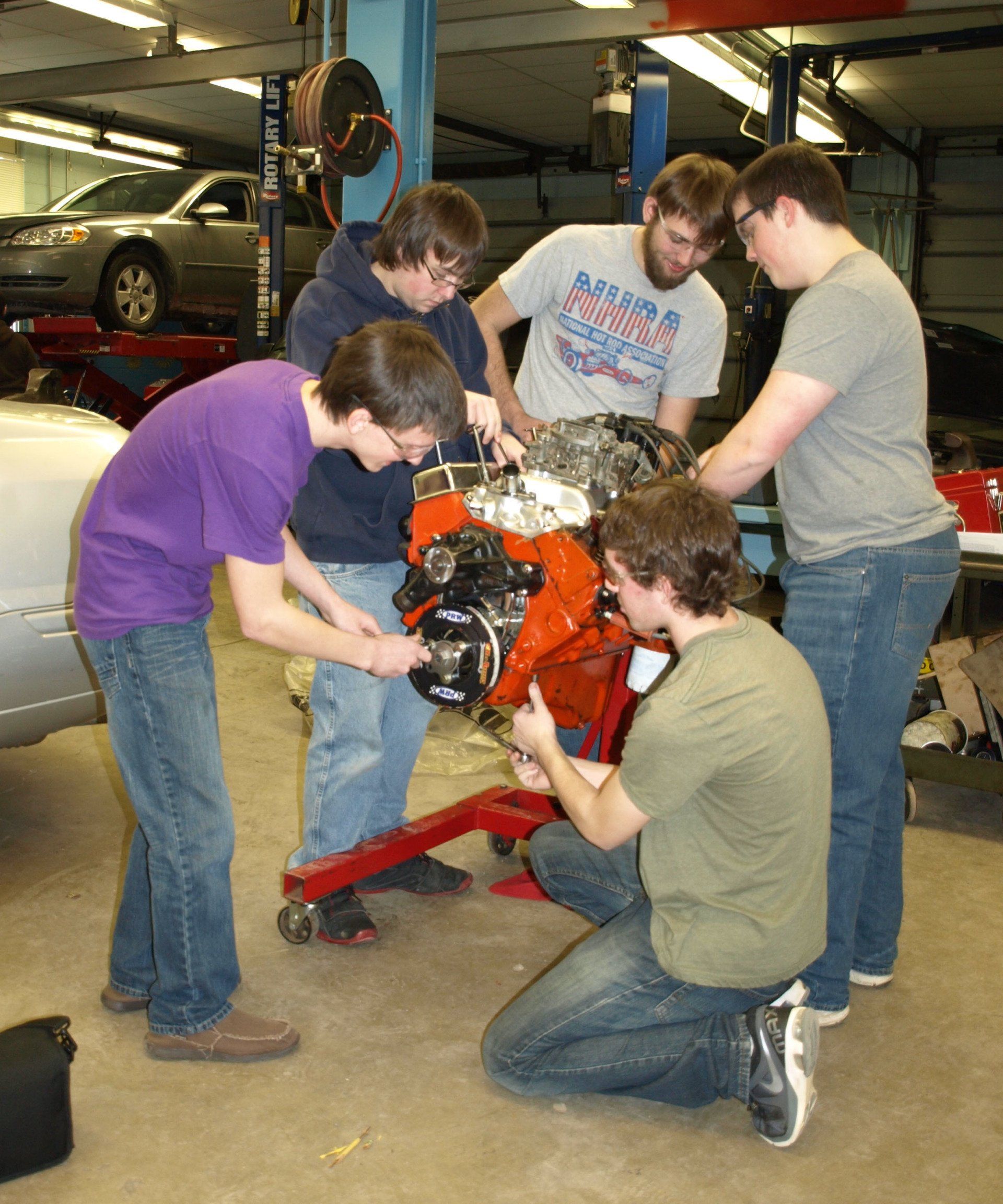 A group of men are working on a car engine in a garage