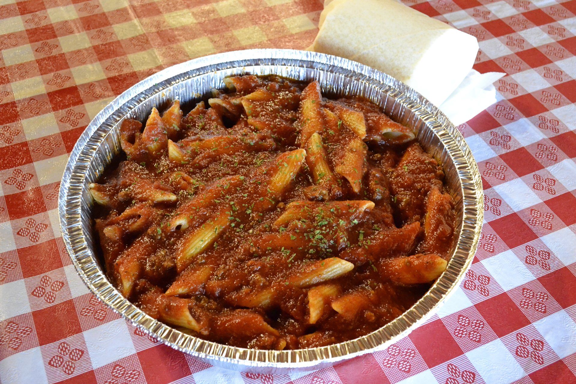 A tin foil container filled with pasta and sauce on a checkered table cloth