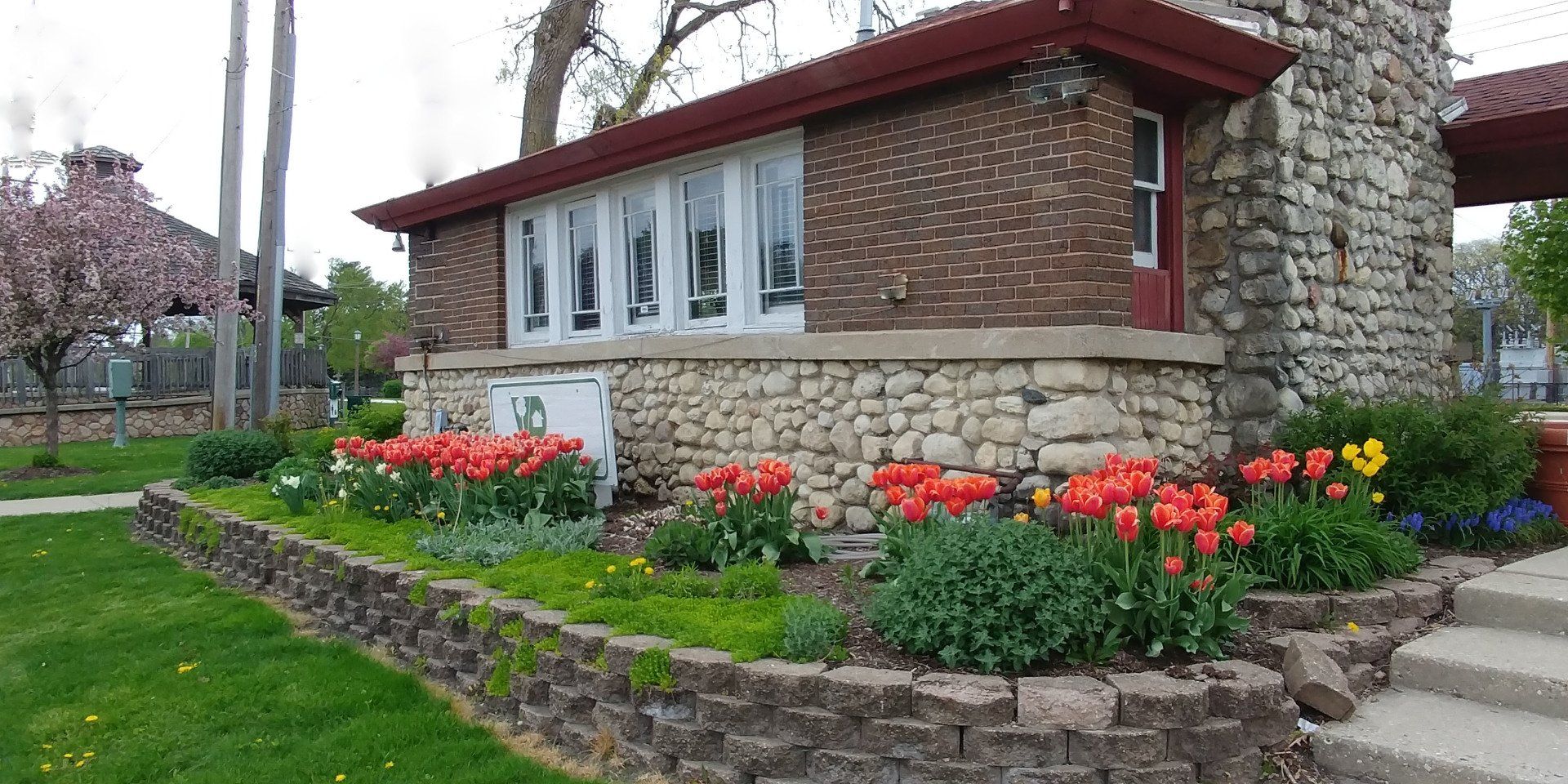 A house with a stone wall and flowers in front of it.