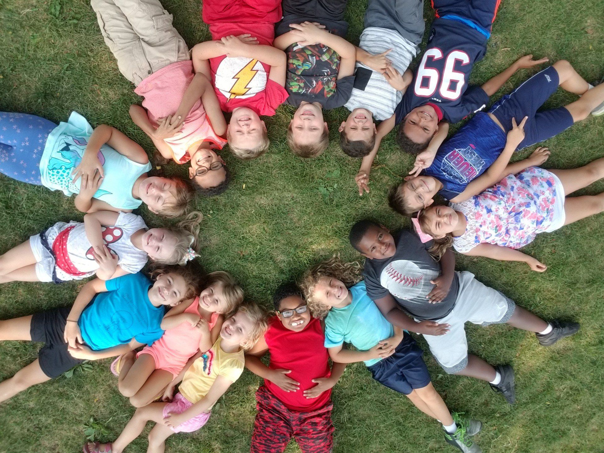 A group of children are laying in a circle on the grass.