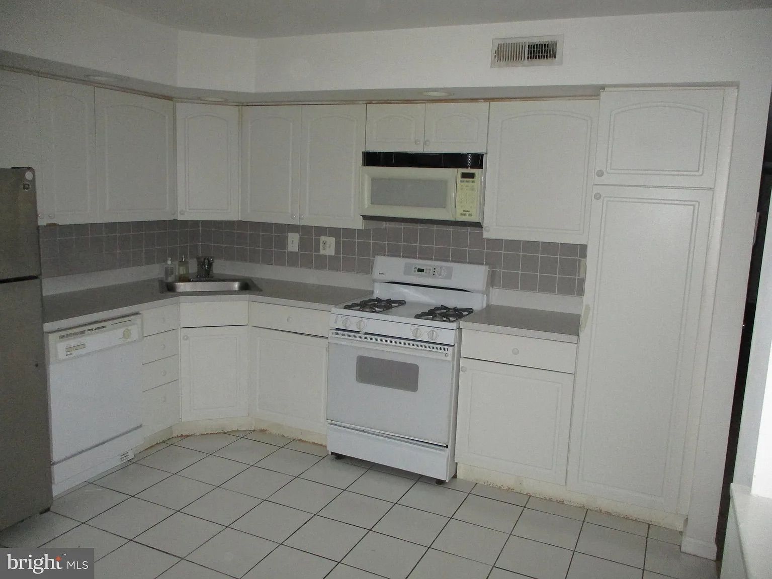 A kitchen with white cabinets , a stove , a refrigerator , and a microwave.