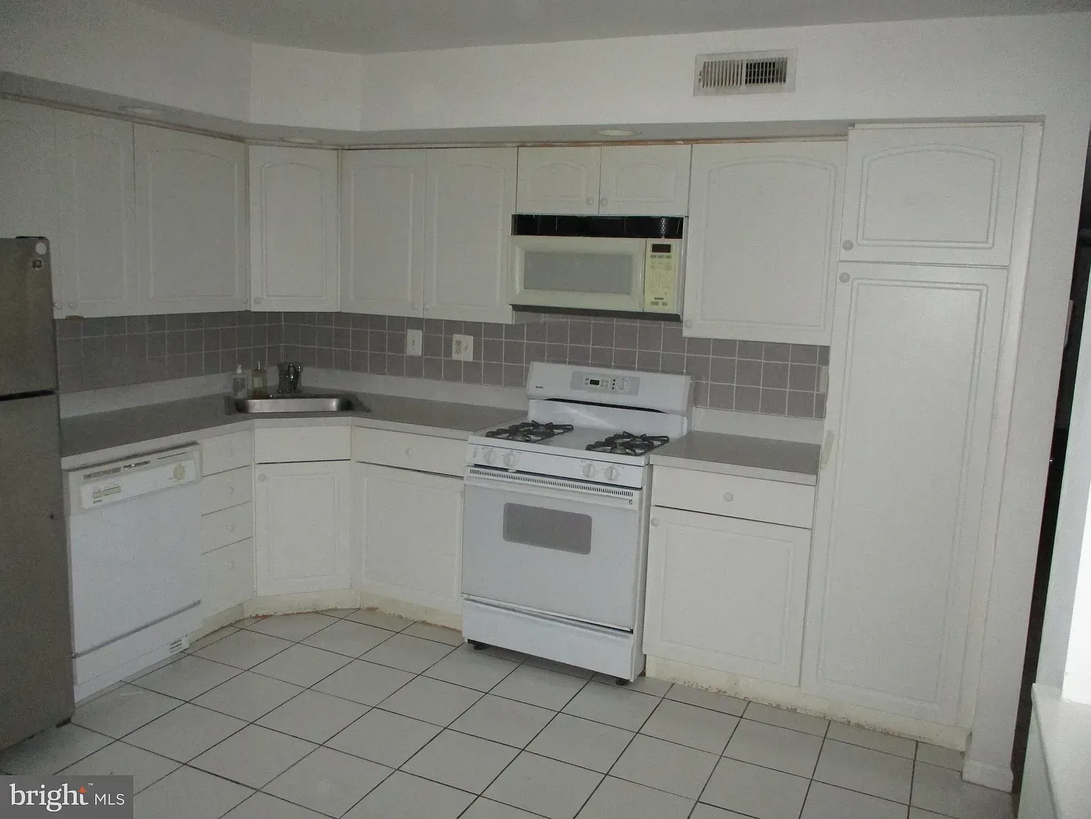An empty kitchen with white cabinets , a stove , a refrigerator , and a microwave.