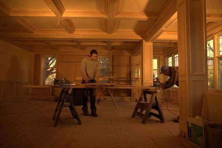 Two men are working on a wooden table in a room.