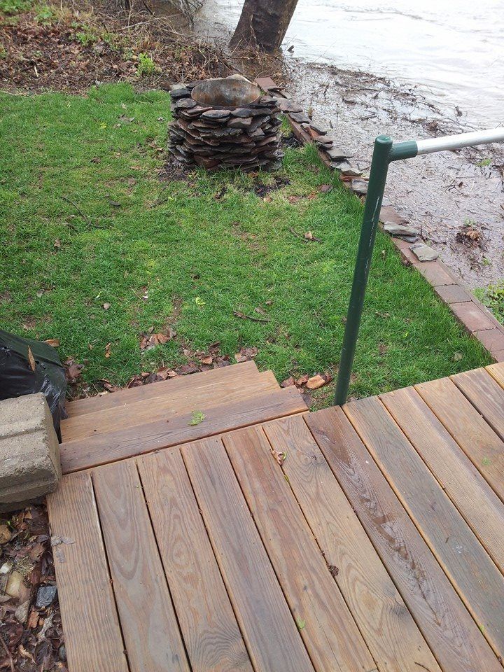 A wooden deck with stairs leading to the water and a green railing.
