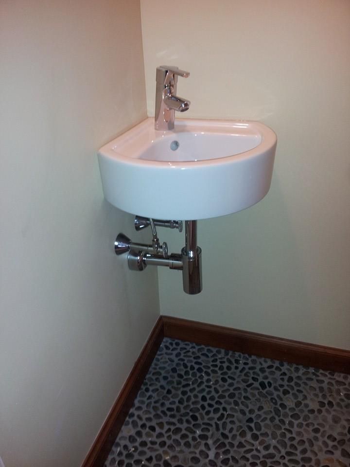A small white corner sink with a chrome faucet