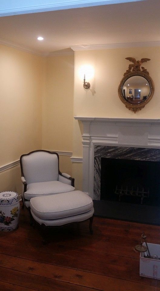 A living room with a fireplace , chair , ottoman and mirror.