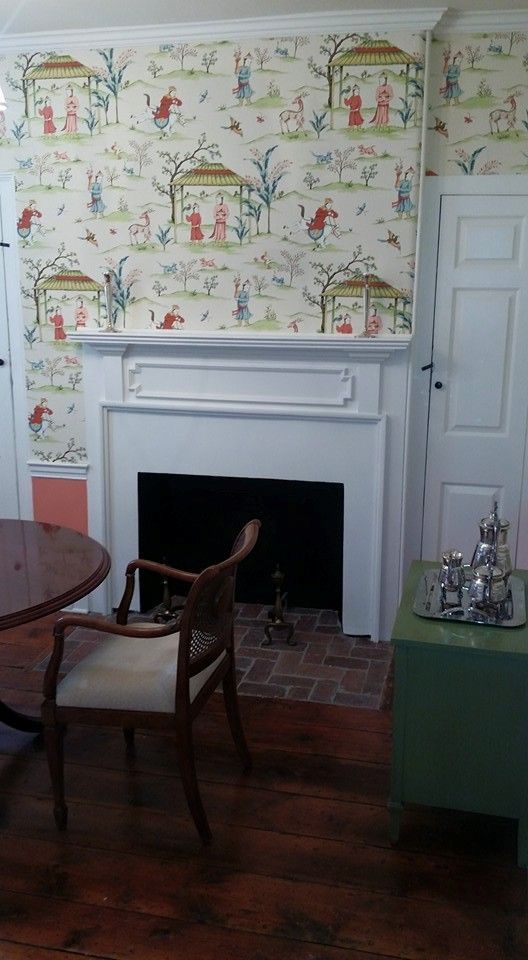 A living room with a fireplace , chair , table and wallpaper.