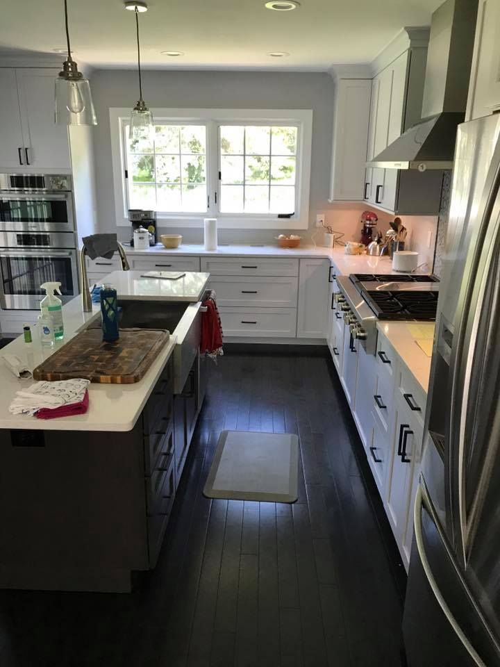 A kitchen with white cabinets , stainless steel appliances , a large island , and a window.