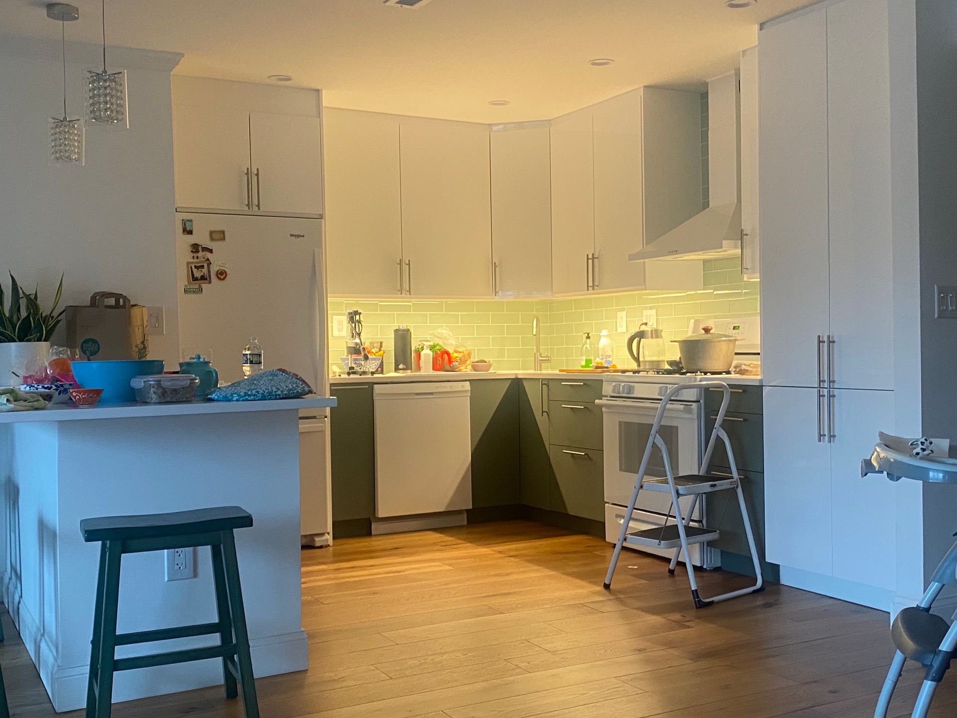 A kitchen with white cabinets , a refrigerator , a stove , a dishwasher and a stool.