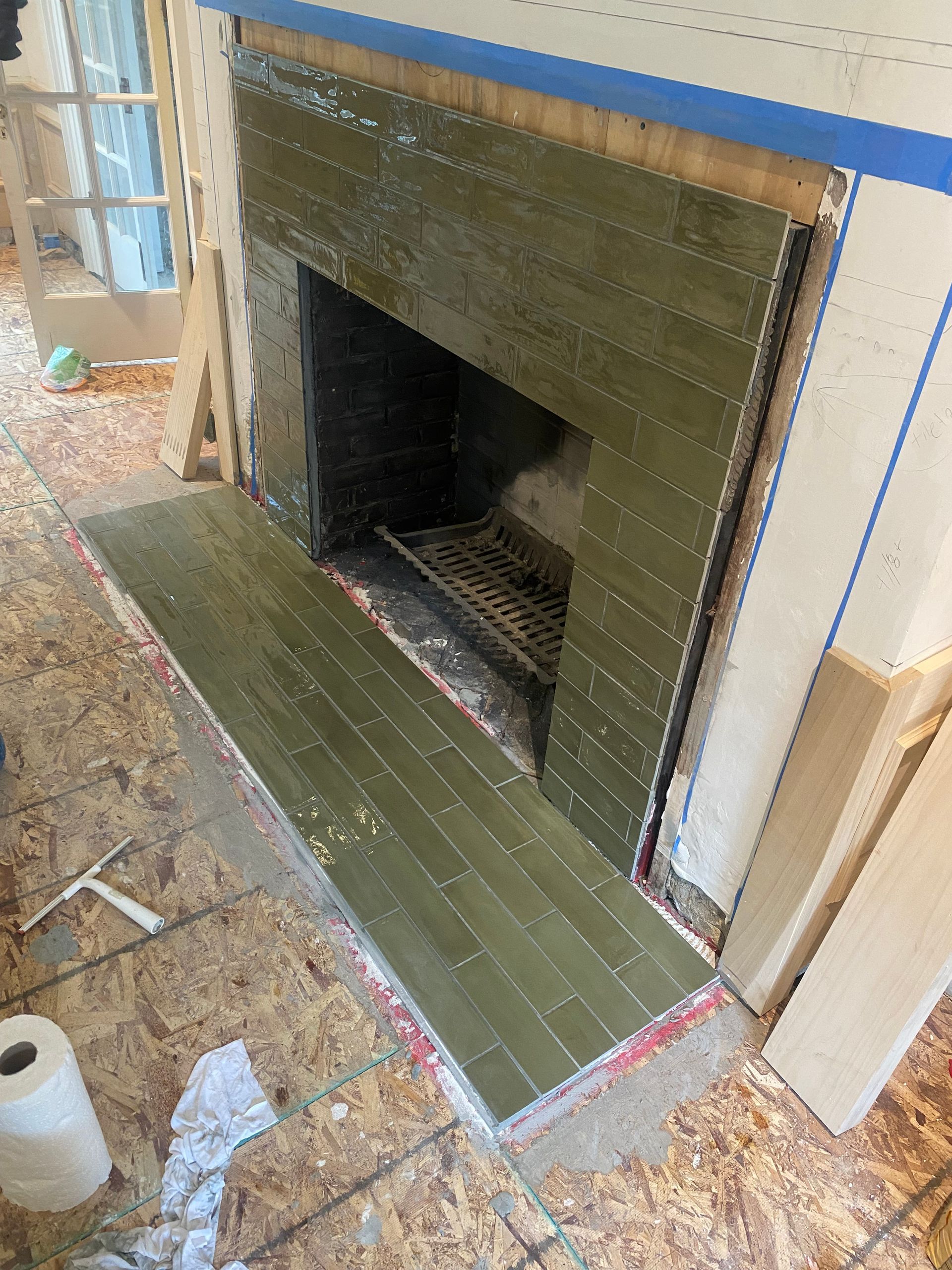 A fireplace with green tiles is being remodeled in a house.