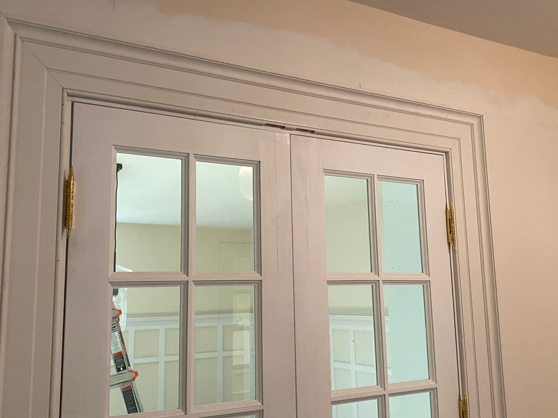 A close up of a white door with a ladder in the background.