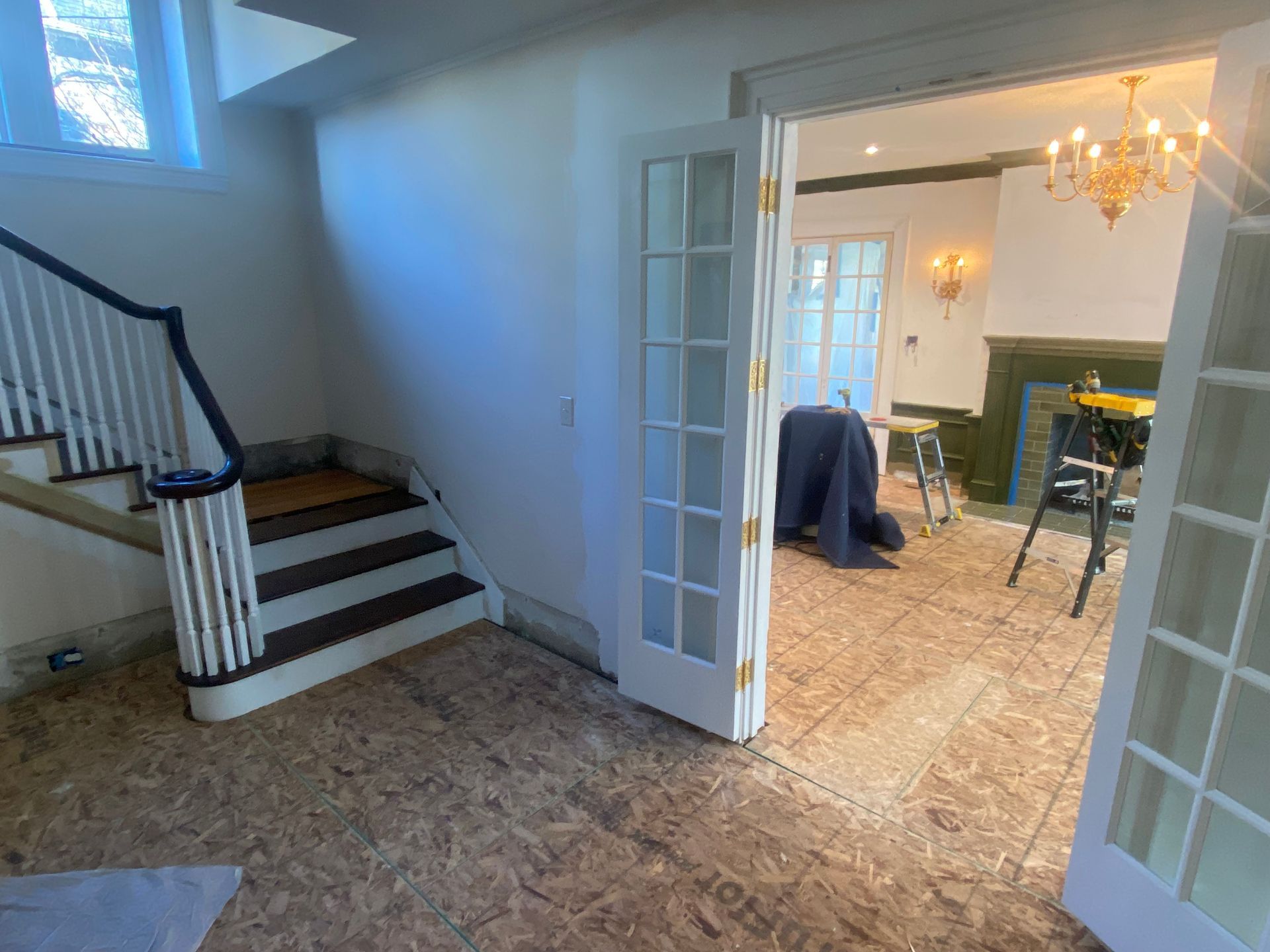 A room with a staircase and french doors leading to a living room.