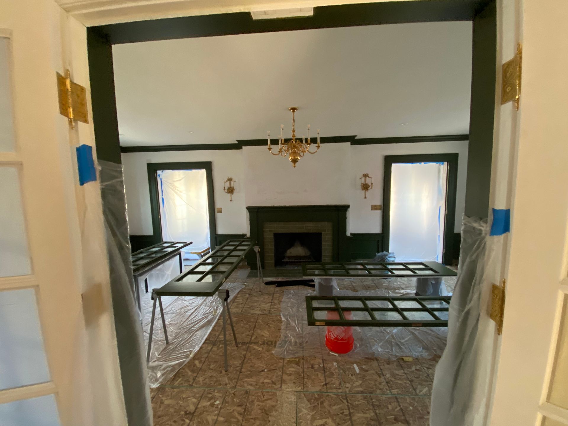 A living room with a fireplace and a chandelier is being painted.