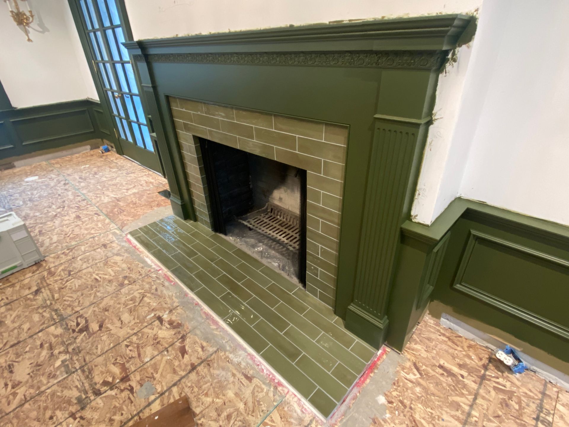 A fireplace with green tiles and a green mantle in a living room.