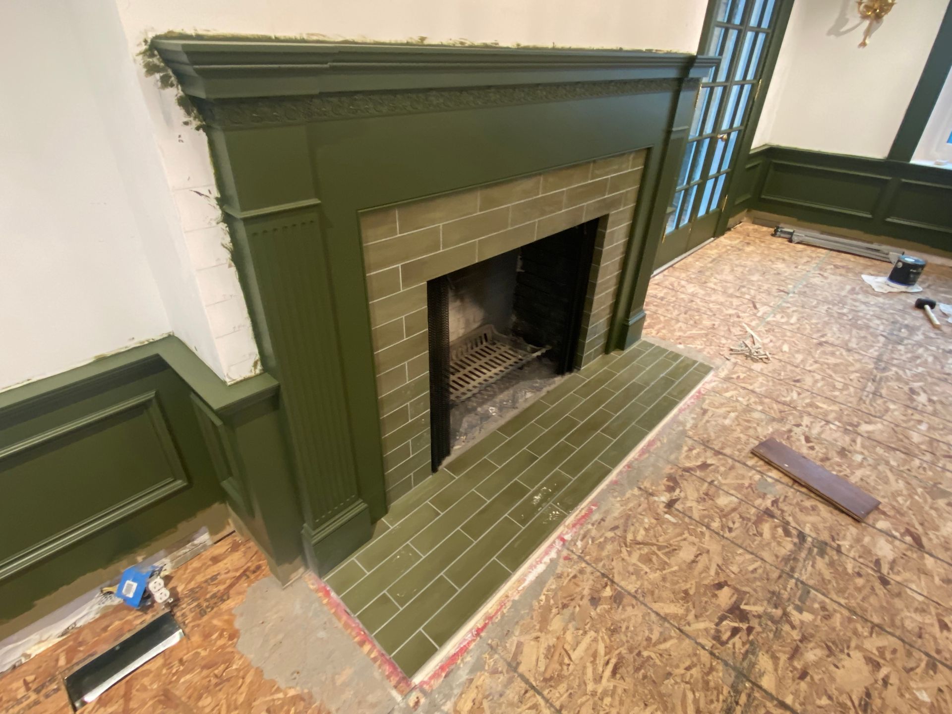 A fireplace is being remodeled in a living room with green trim.