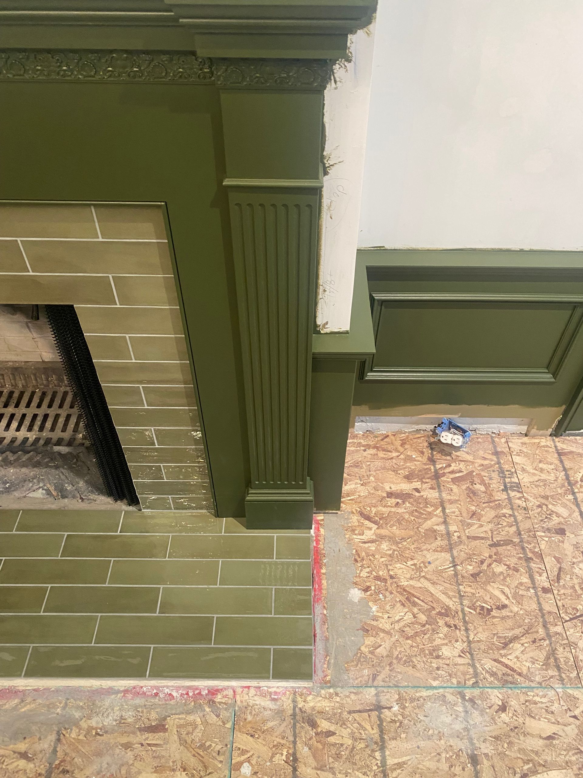 A fireplace with green tiles and green trim in a room.