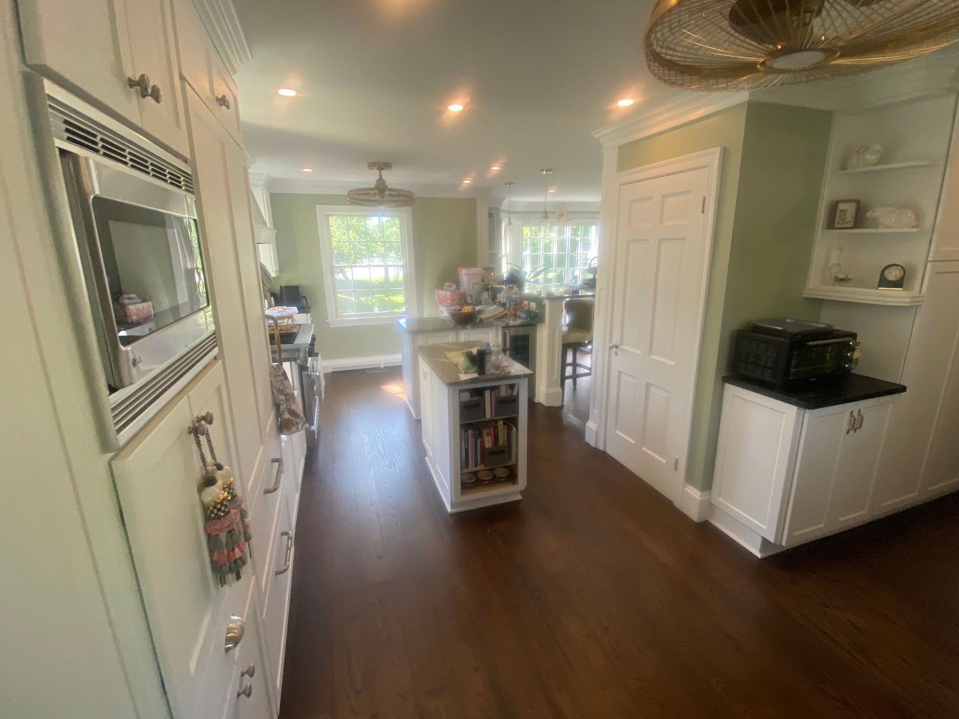 A kitchen with white cabinets , hardwood floors , a microwave , and a ceiling fan.