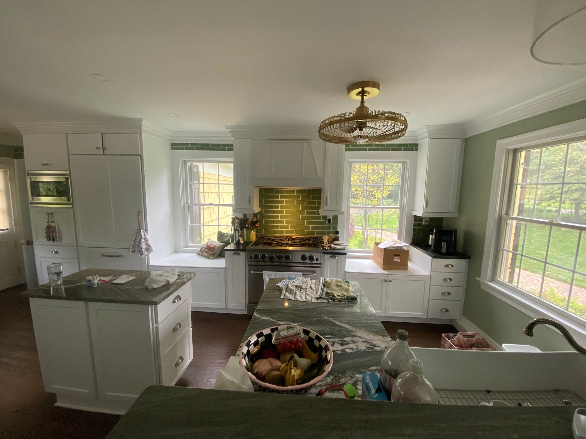 A kitchen with white cabinets , a stove , a sink , and a bowl of fruit on the counter.