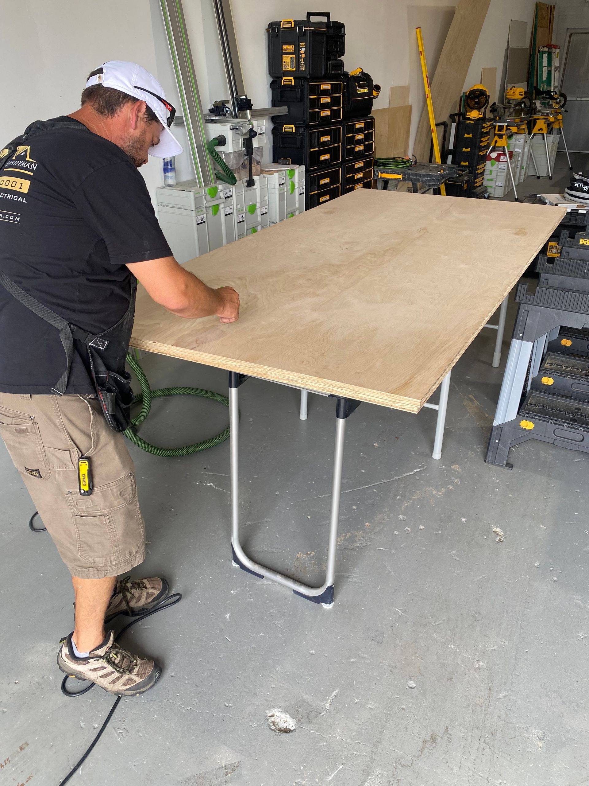 A man in a black shirt is standing next to a wooden table