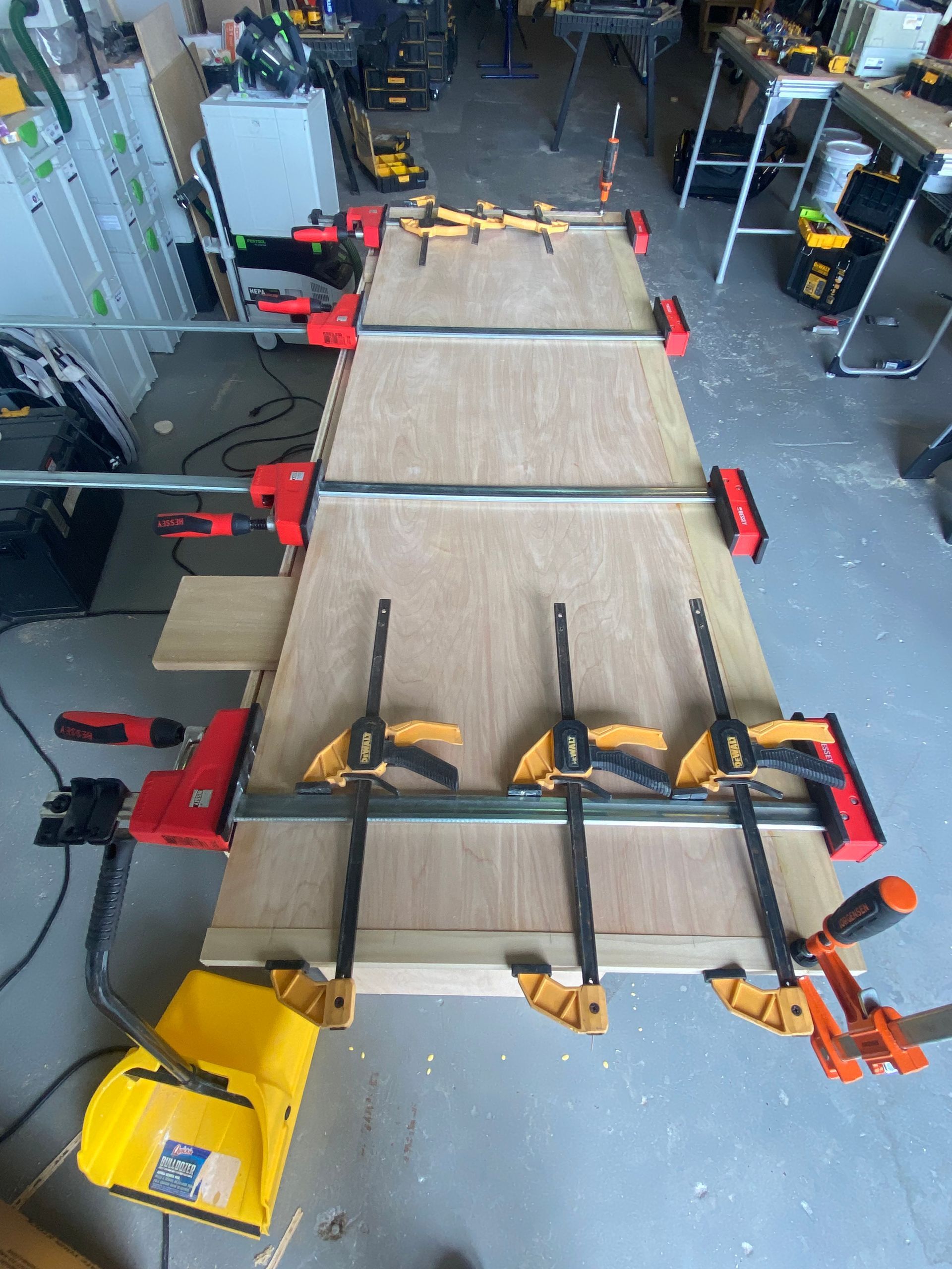A wooden table is being held together with clamps in a garage.
