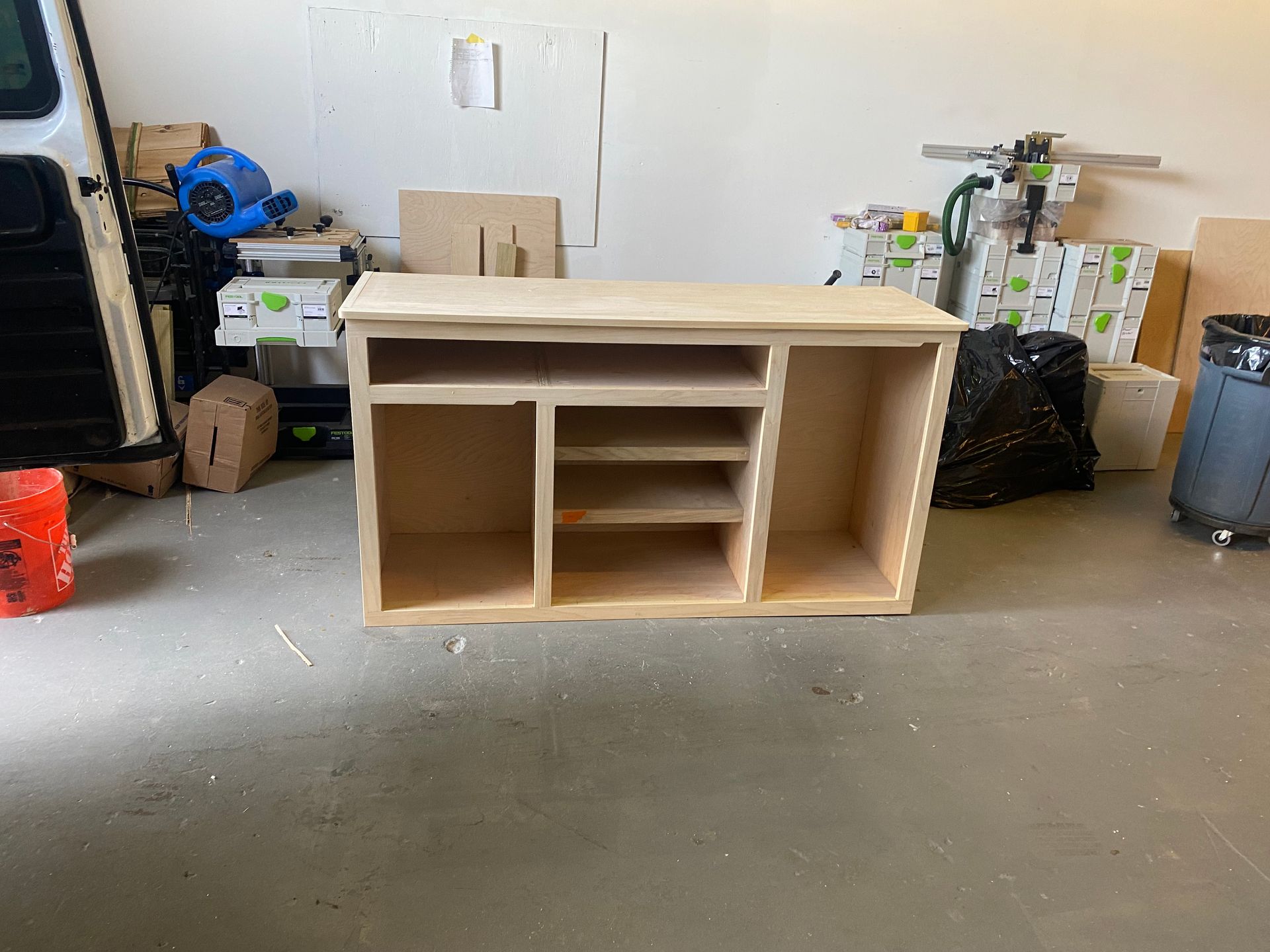 A wooden cabinet is sitting in a garage next to a van.