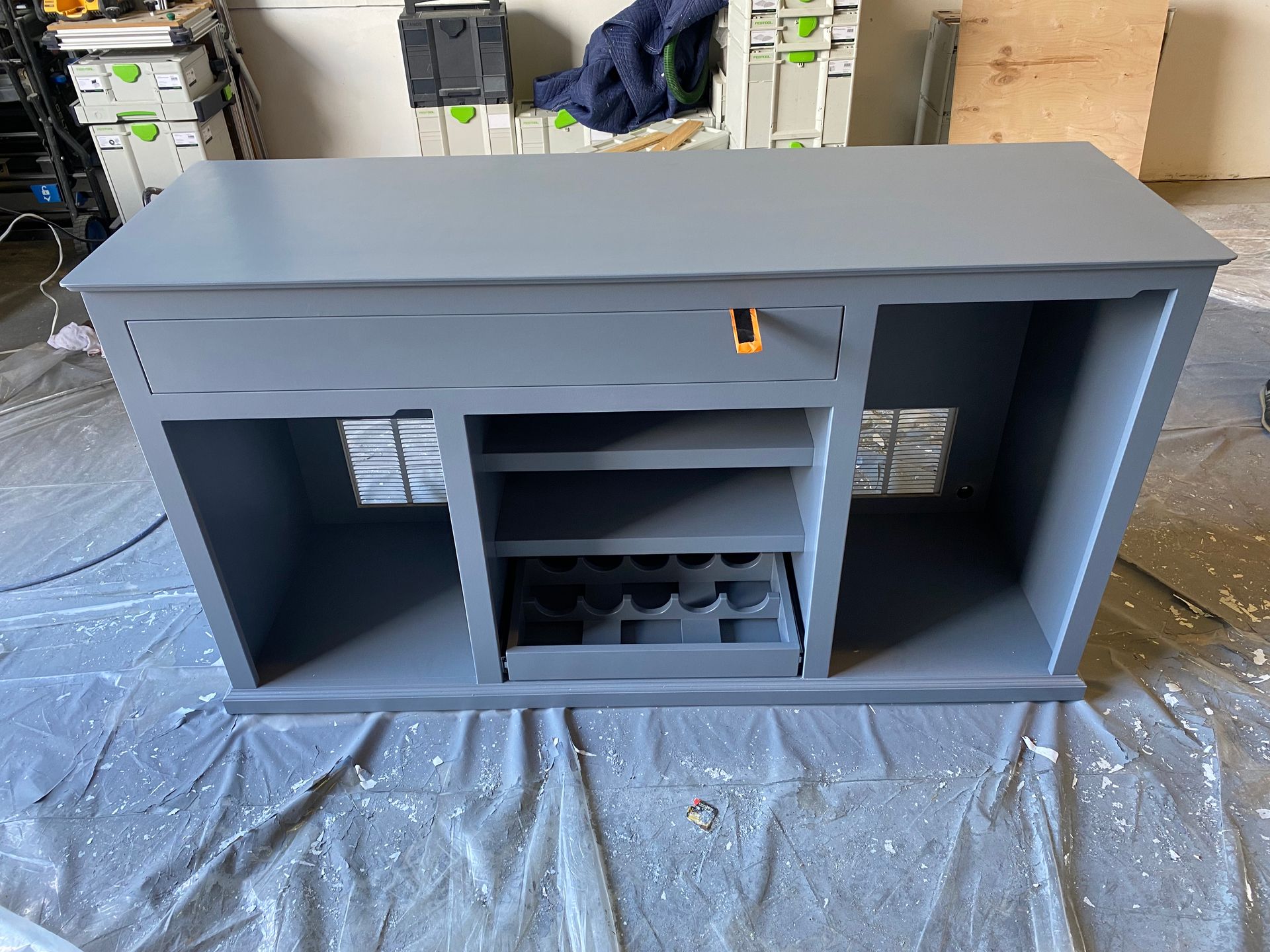 A gray table with a drawer and shelves is sitting on a table covered in plastic.