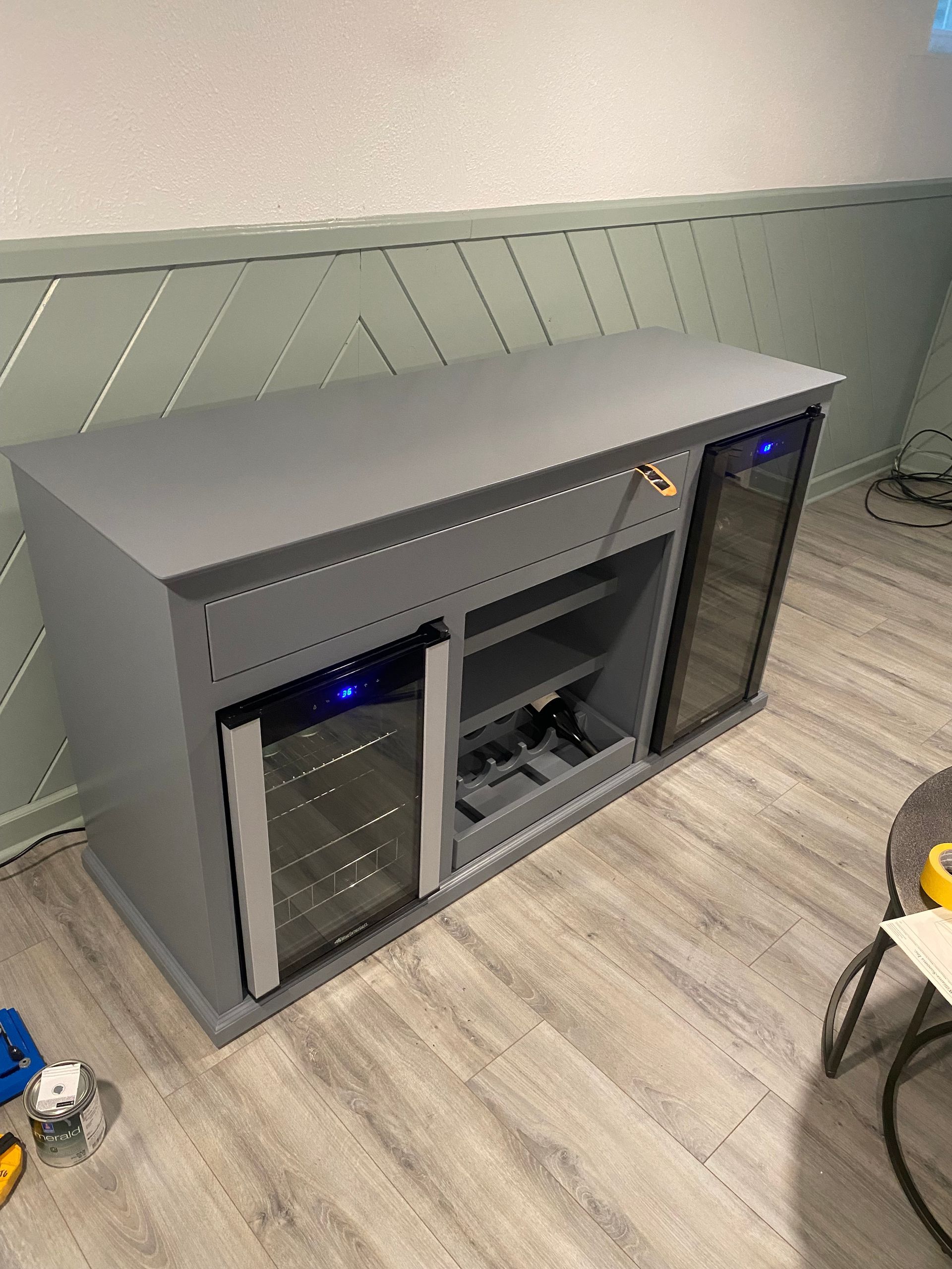 A gray cabinet with a wine cooler inside of it is sitting on a wooden floor.