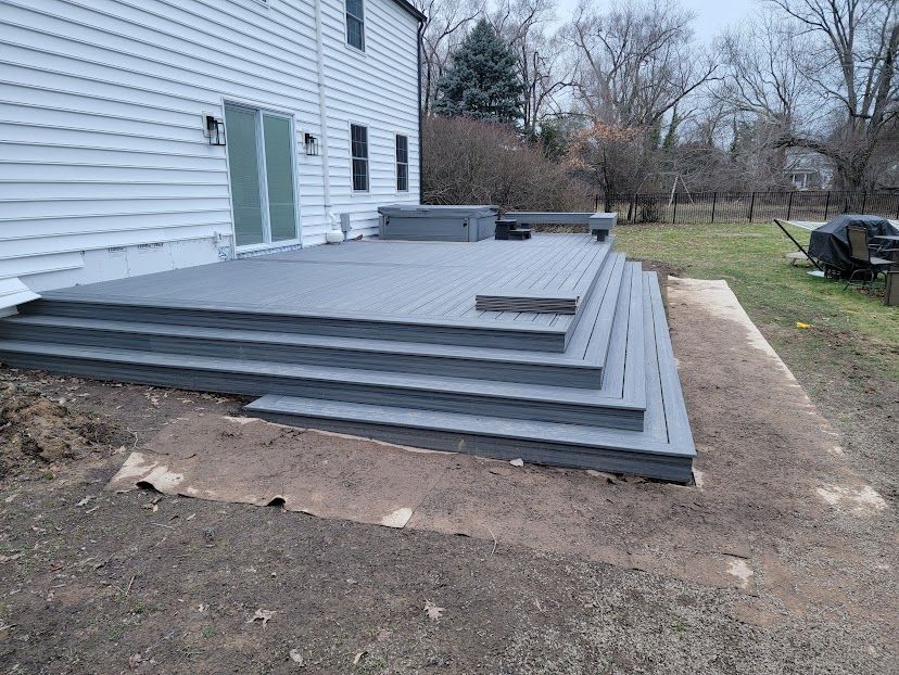 A large gray deck with stairs is in front of a white house.