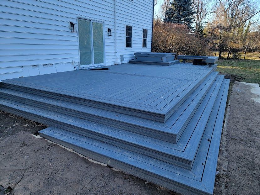A gray deck with stairs leading up to it is in front of a white house.