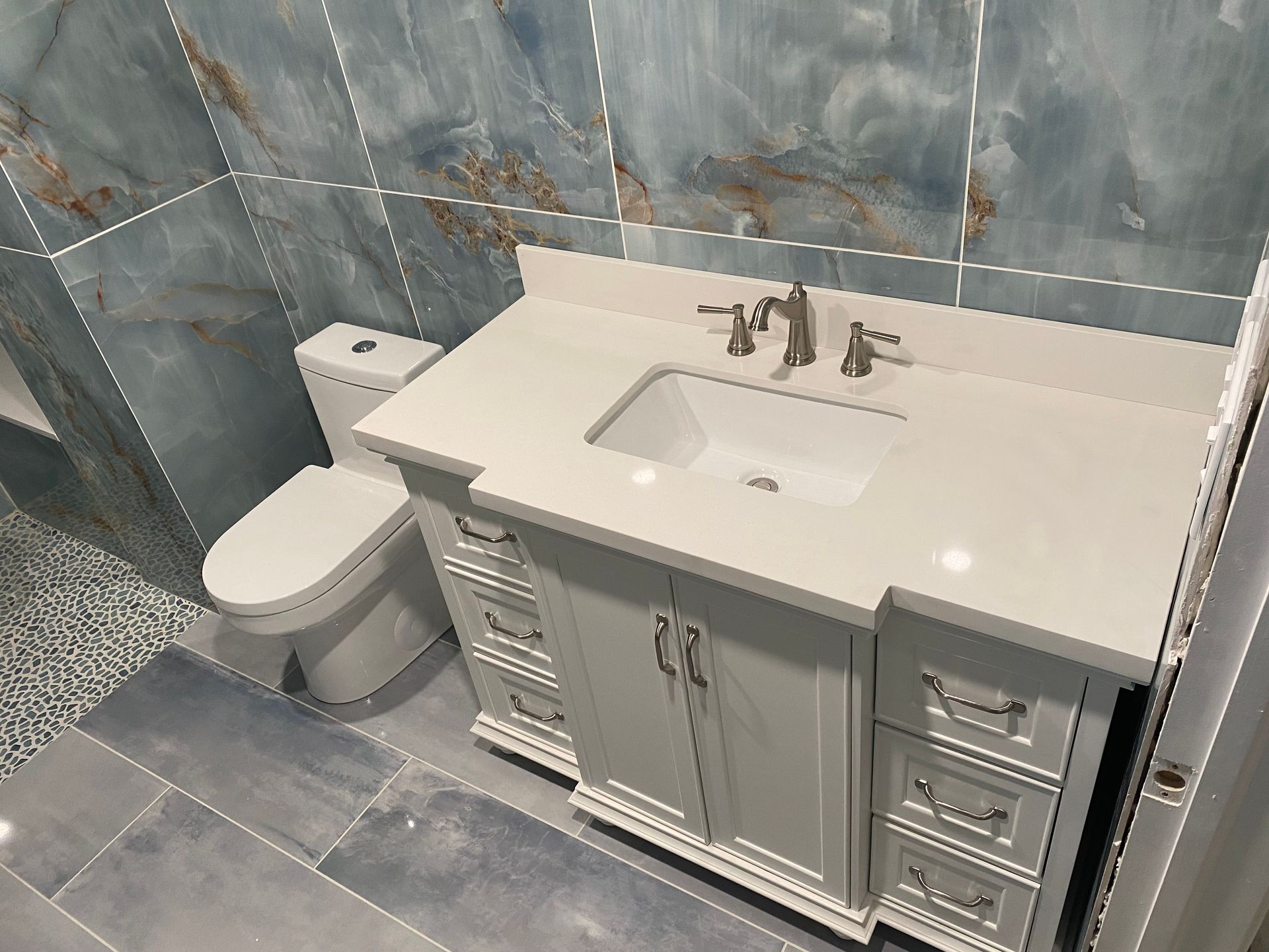 A bathroom with a sink , toilet and blue tiles.