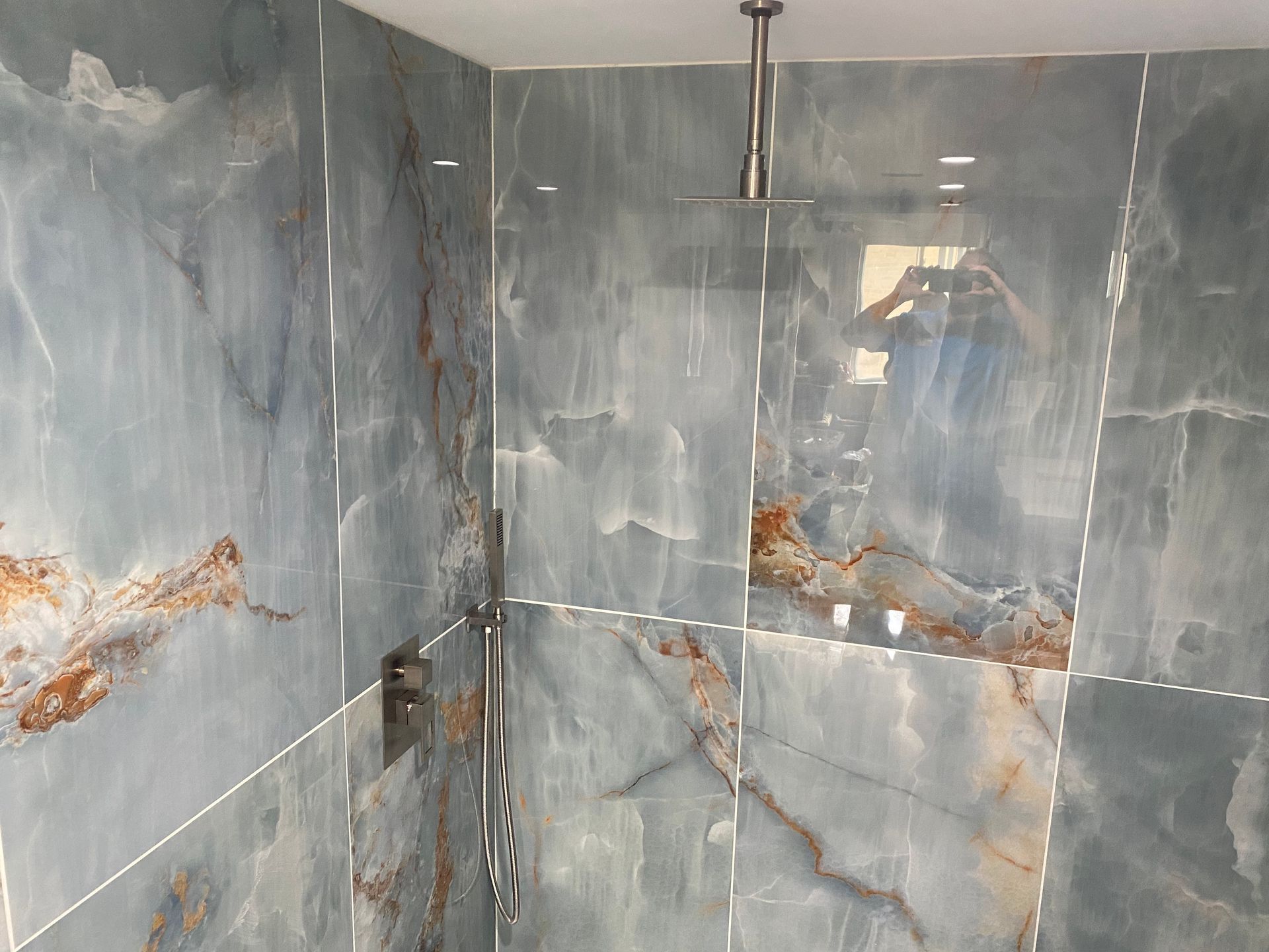 A bathroom with blue tiles and a shower head.